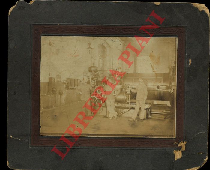 - - Interno d'officina con macchina utensile a vapore e tre operai addetti.